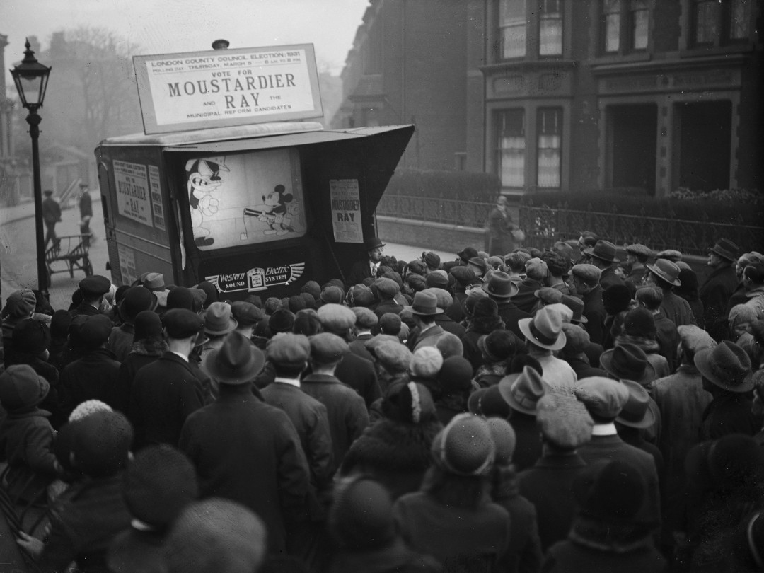 Mickey Mouse is shown on a small screen in a city street, London, 1931