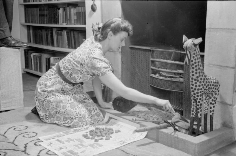 Mrs Olive Day nettoie le foyer de la cheminée, elle met de coté les charbons pour les réutiliser.
