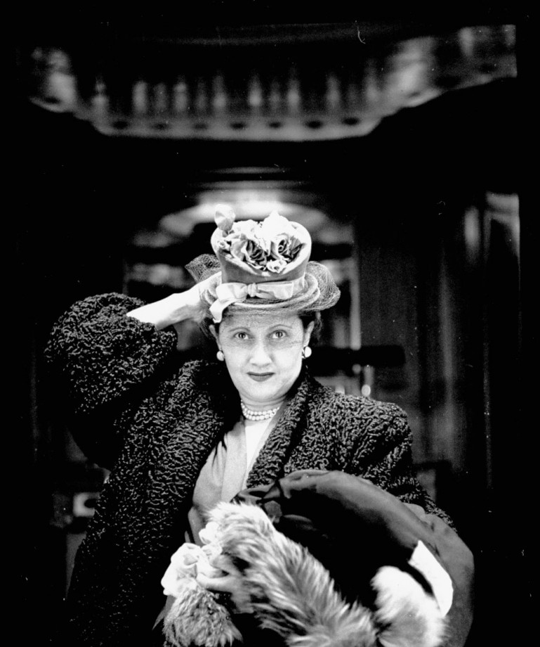 Woman adjusting flowered hat while looking in tric